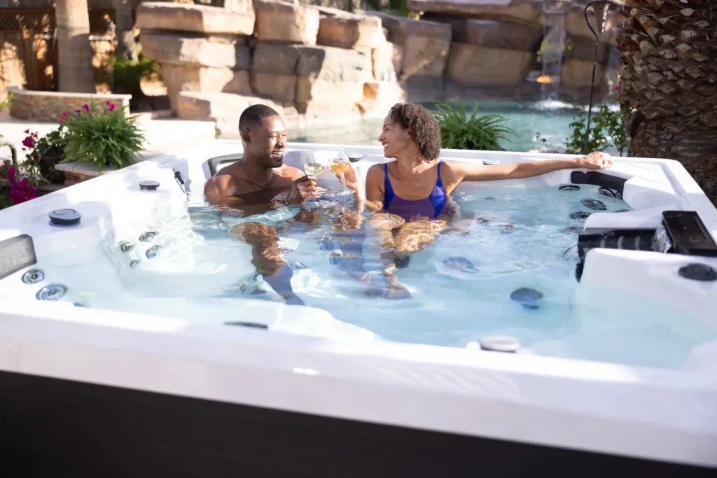 Couple enjoying a relaxing moment in a hot tub with hydrotherapy jets, surrounded by lush greenery and a serene water feature, highlighting the customizable spa experience offered by Creative Hot Tub Designs in Reno NV and Sparks NV.