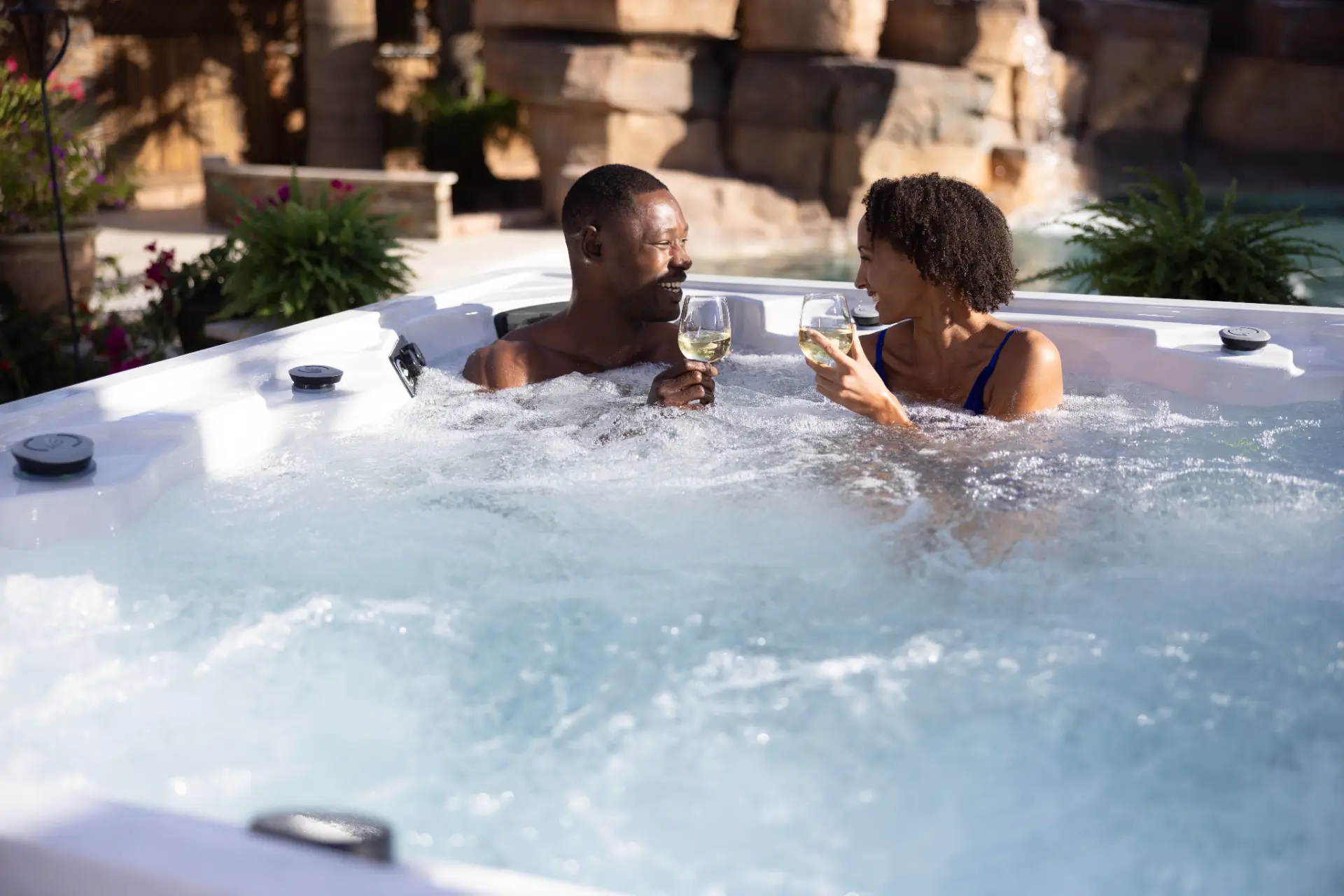 Couple enjoying drinks in Artesian Spa hot tub, surrounded by lush greenery, showcasing luxury relaxation experience from Creative Hot Tub Designs in Reno NV.