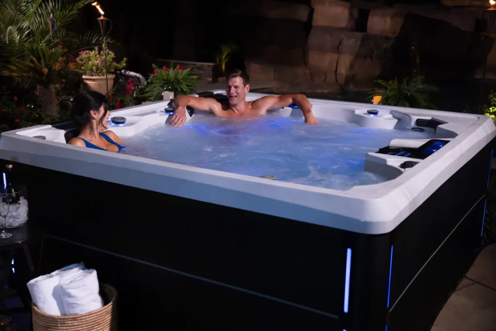 Couple enjoying luxury Artesian Spa hot tub with illuminated water features, emphasizing relaxation and wellness in a serene outdoor setting, highlighting Creative Hot Tub Designs in Reno, NV and Sparks, NV.