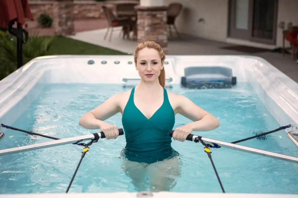 Woman exercising in TidalFit® Swim Spa, using resistance bands for aquatic fitness, showcasing luxury backyard oasis by Creative Hot Tub Designs in Reno, NV.