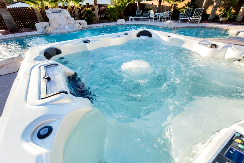 Hot tub with hydrotherapy jets and bubbling water, showcasing Artesian Spas™ features, set in a relaxing outdoor environment with a pool and lounge chairs, emphasizing wellness and customizable spa experiences in Reno, NV.