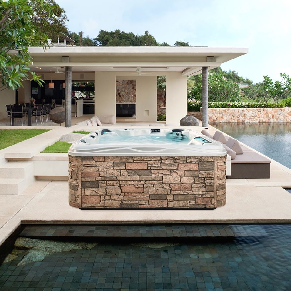 Hot tub with sandstone rock cabinetry in outdoor setting, surrounded by modern architecture and lush greenery, showcasing Creative Hot Tub Designs' commitment to stylish and accessible spa solutions in Reno NV and Sparks NV.
